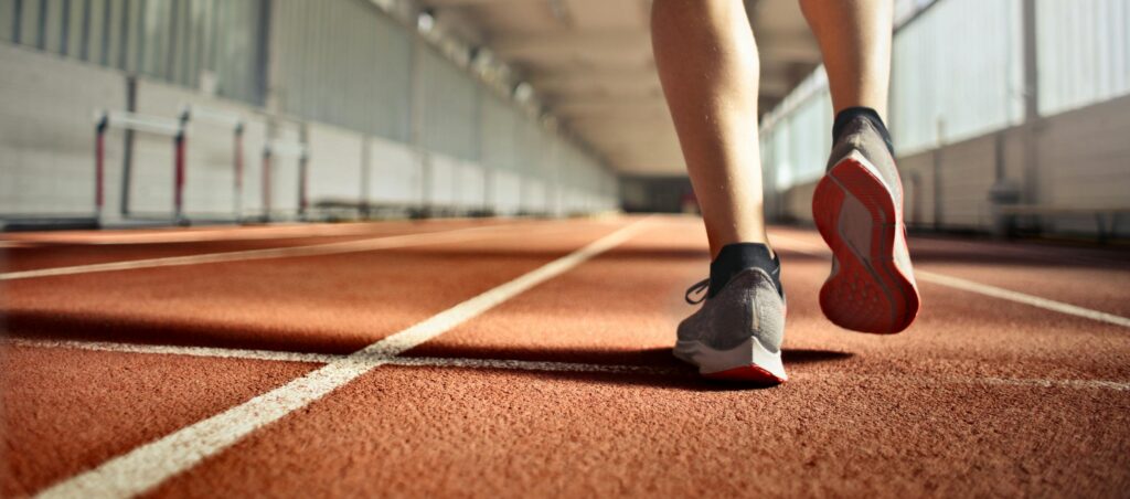 Photography taken from below of the back view of person walking along a running track in athletics stadium